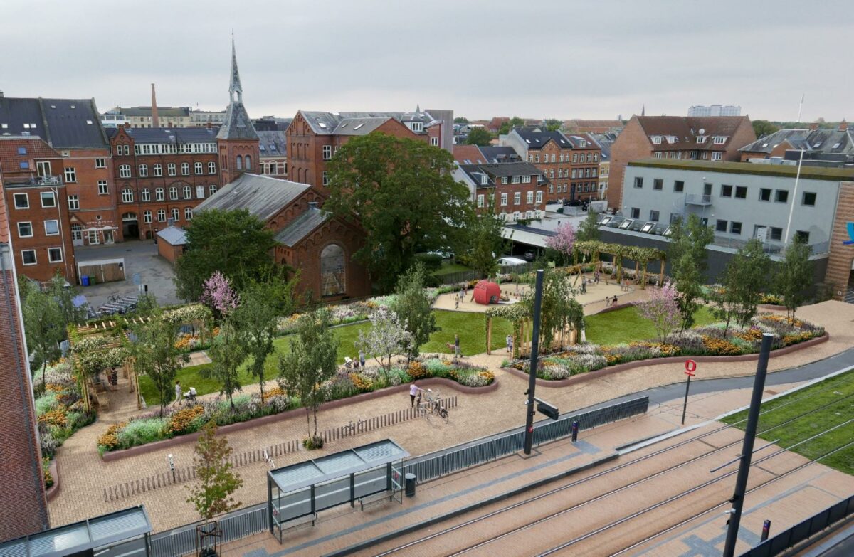 Med den nye lommepark ved Vestre Stationsvej får det centrale Odense et nyt grønt frirum, der spiller sammen med kirkens nye bemalede glasrude, der vender ud mod parken. Illustration: Land+