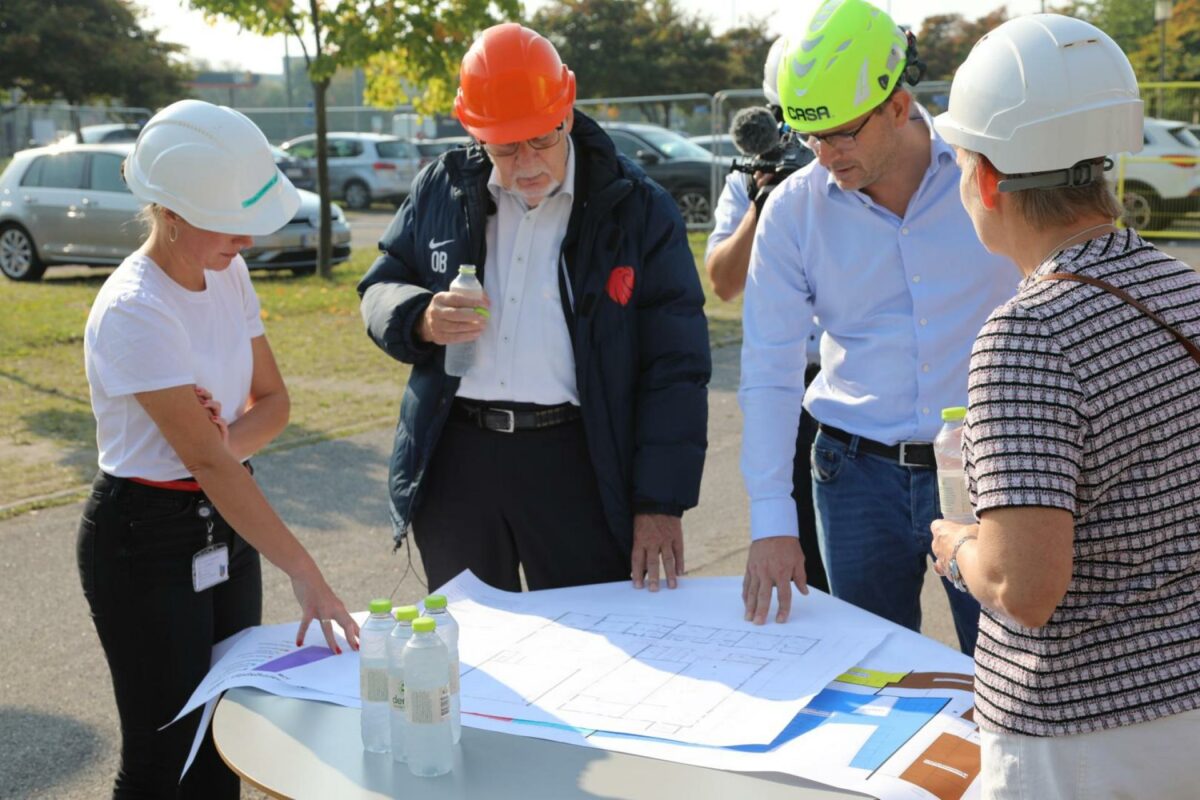 John Strands Petersson fra Casa (gul hjelm) fremlægger byggeplanerne for borgmester Ole Bjørstorp (orange hjelm), teknik- og miljødirektør Marie Louise Madsen (tv) og Inge Sørensen (th), der er chef for Center for Ejendomme i Ishøj Kommune. Pressefoto.