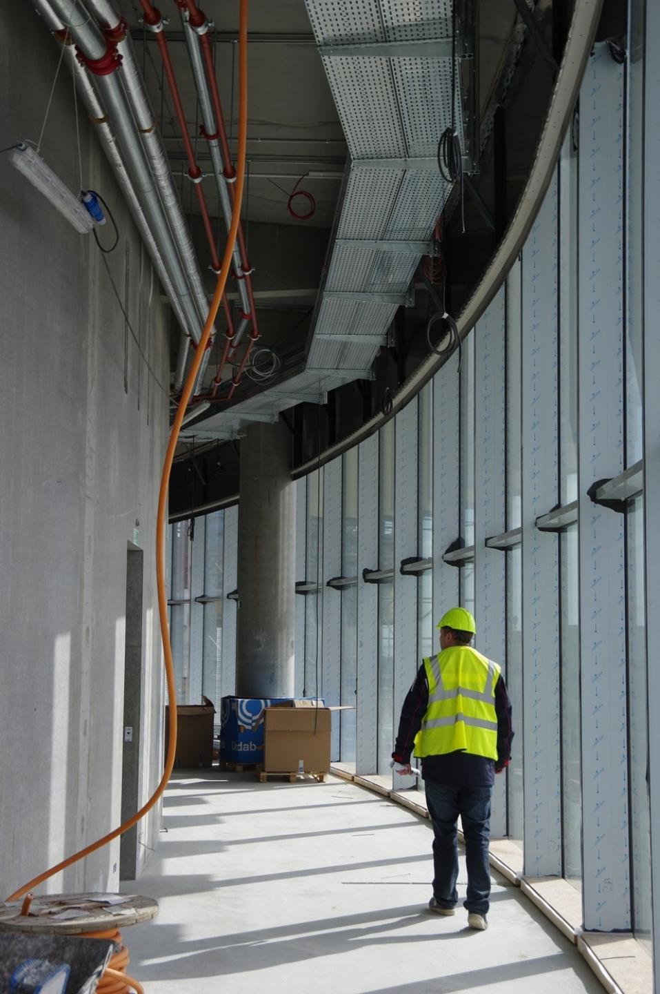 Skou Gruppen har monteret skørter på siden af alle betondæk. Skørterne skjuler installationerne, så de ikke ses gennem arenaens glasfacader. Efterfølgende monteres akustikpladerne i loftet. Foto: Skou Gruppen.