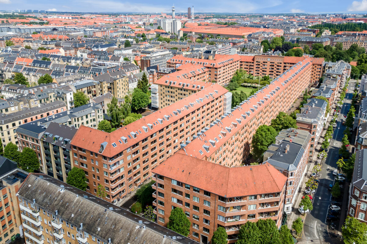 Luftfoto af den enorme, sammenhængende bebyggelse Hostrups Have i røde tegl, rødt tag og grønt både i midten af den aflange bebyggelse og omkring