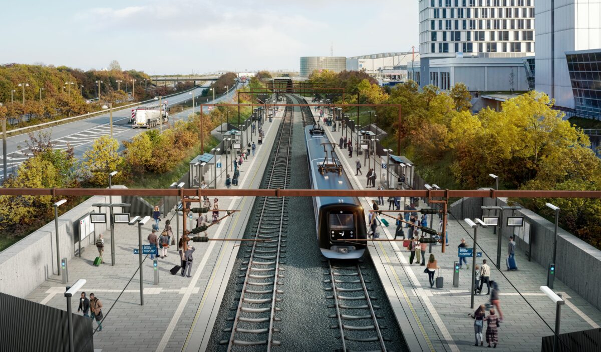 Visualisering afstation med to spor. Et tog holder i den ene side. Stationen ses fra en bro. Der er grønne træer på begge sider af perronerne og masser af rejsende, der venter på tog