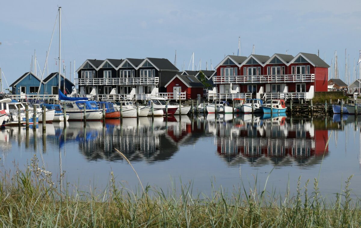 Foto af boliger bygget lige ved havnekanten i Grenaa. De otte røde og hvide huse i to etager ligger fire og fire og spejler sig i havnens vand. Der ligger sejlbåde ved kaj foran boligerne