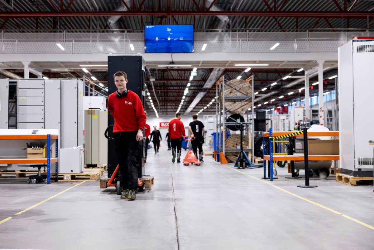 En ung mand i en rød sweatshirt trækker en palle med en stor, sort eltavle. Bag ses mere lager