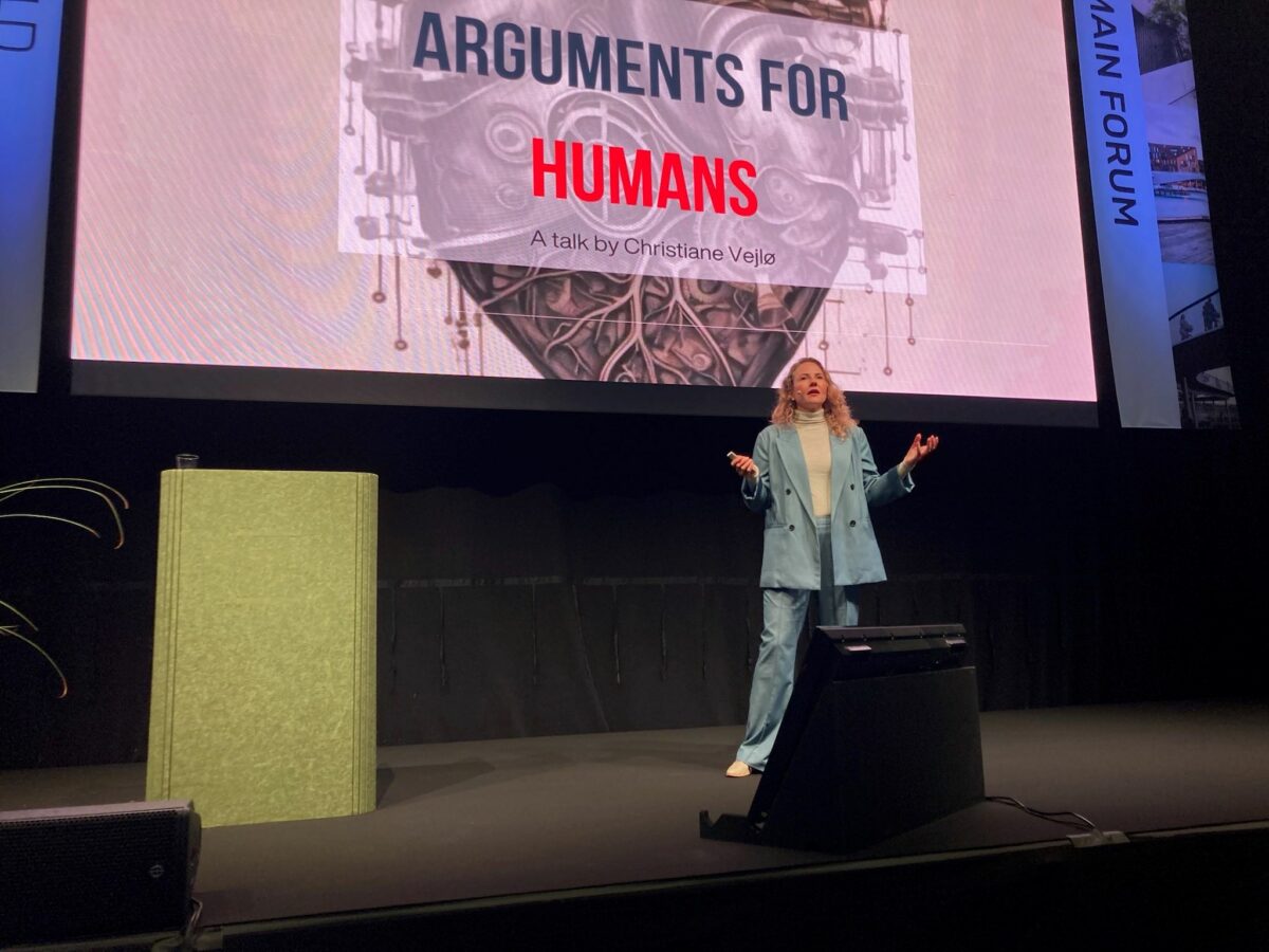 Christiane Vejlø står på en scene og taler. På skærmen bag hende står "Arguments for humans".