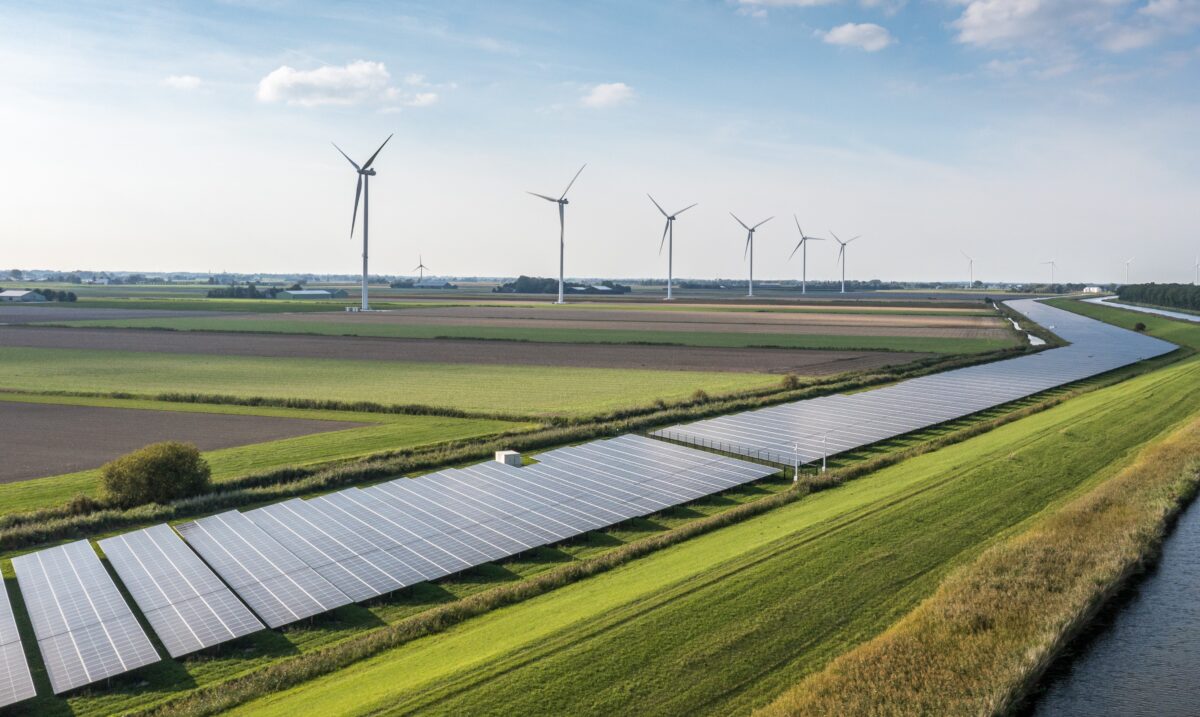 Stort grønt område med solceller og vindmøller i baggrunden.