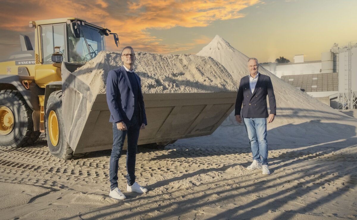 To mænd står foran en gul gravko. Himlen bag er flot med gult lys i skyerne